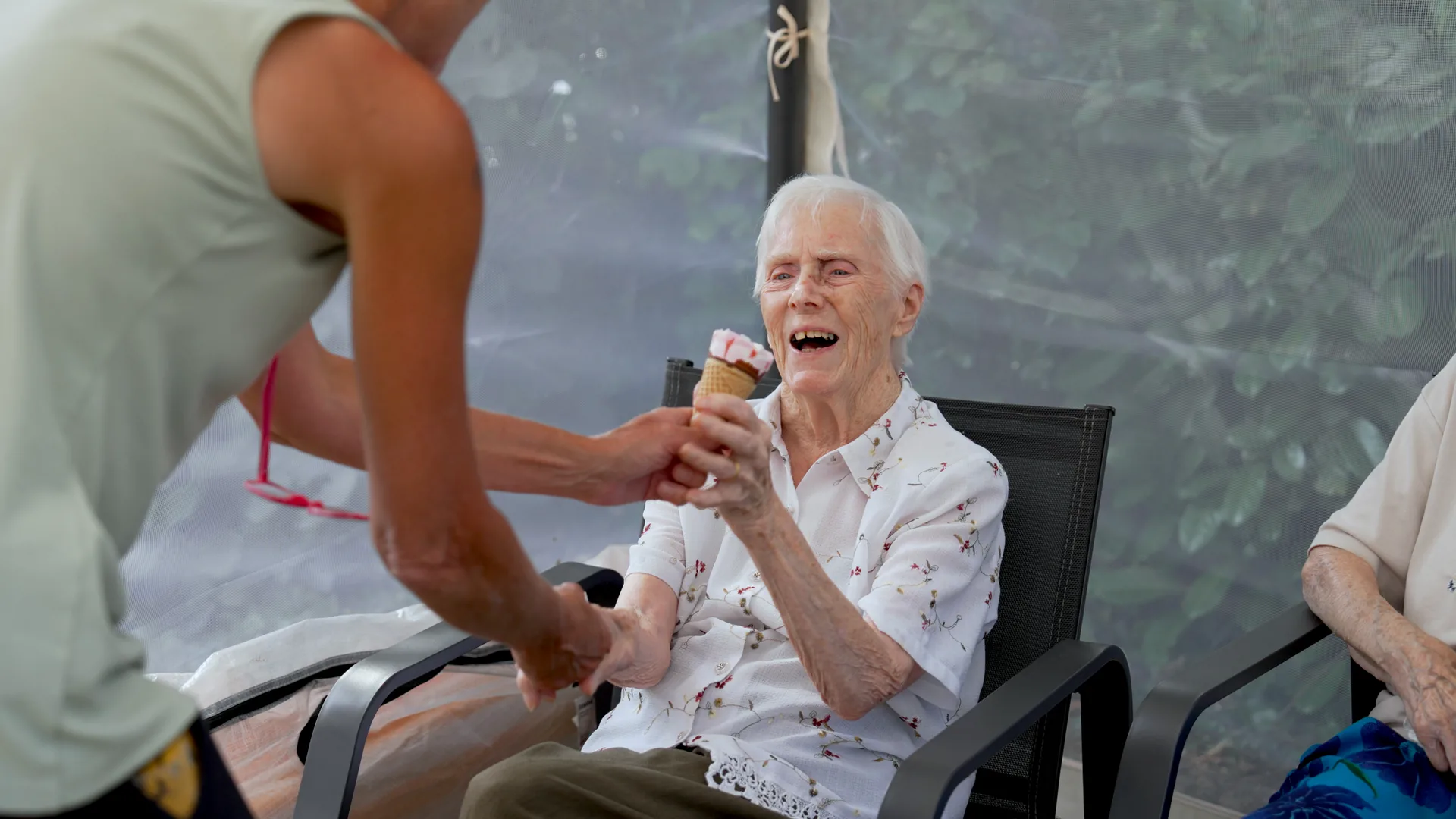 A carer serving ice cream to a laughing resident in a care home.
