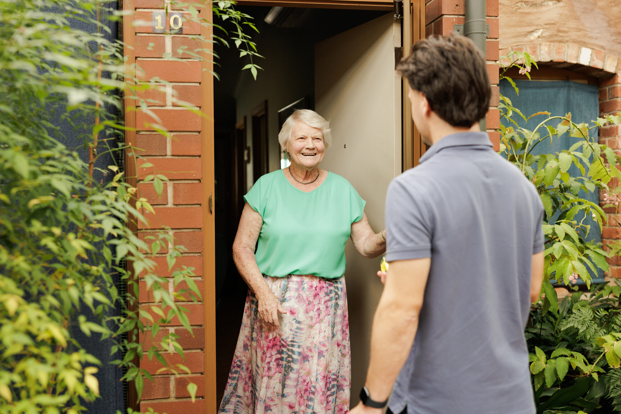 A resident at the door being welcomed by a care assistant.