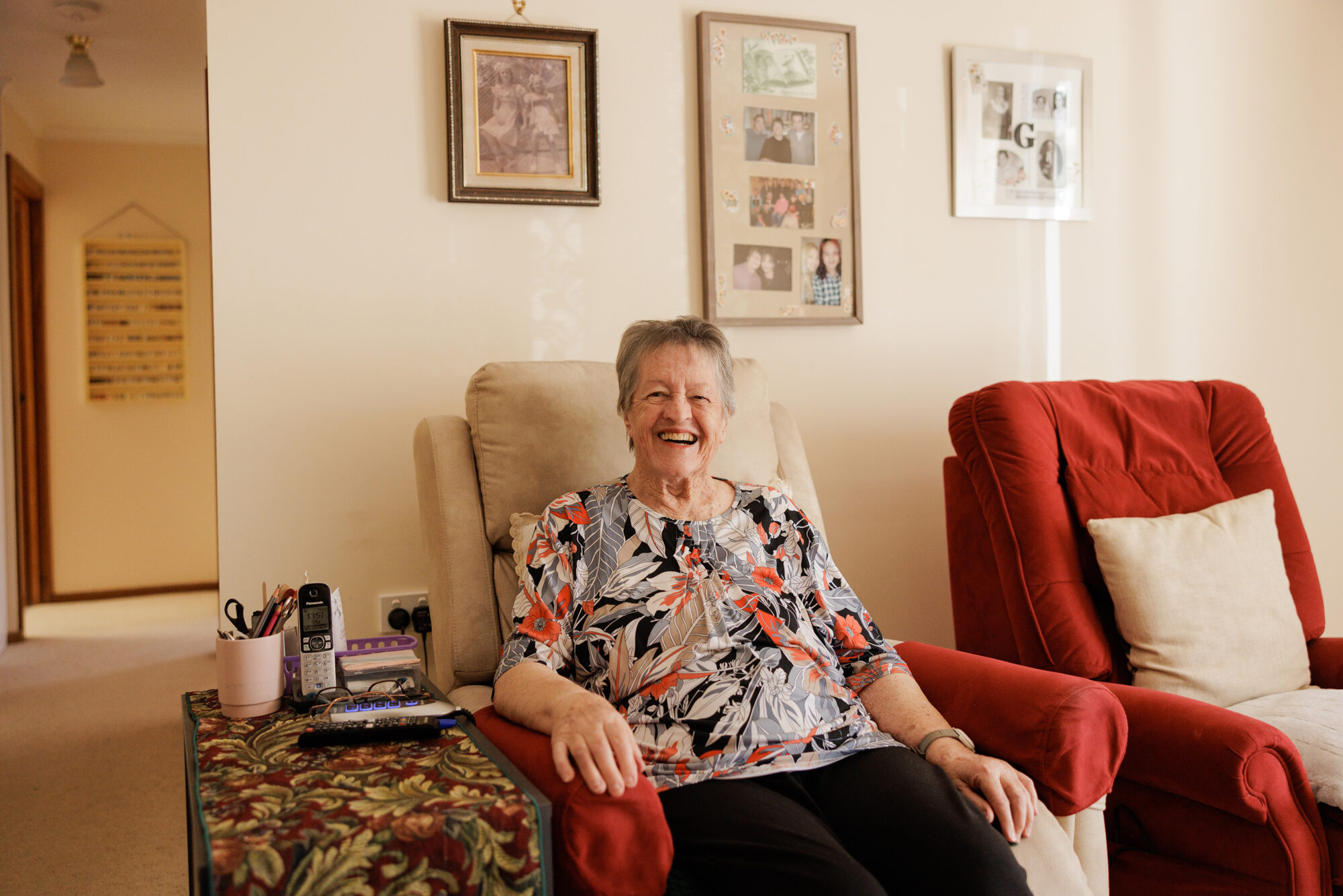 A resident laughing warmly in her armchair at home.